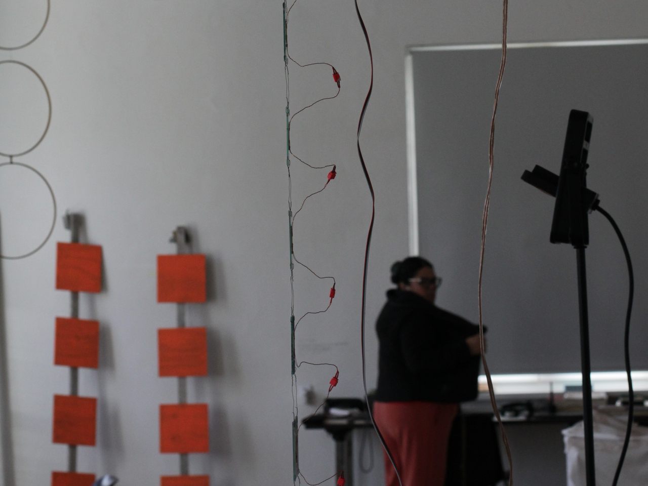 different suspended objects: wooden rings on the left, wooden red square panels in back, glass slides and cables in the front right