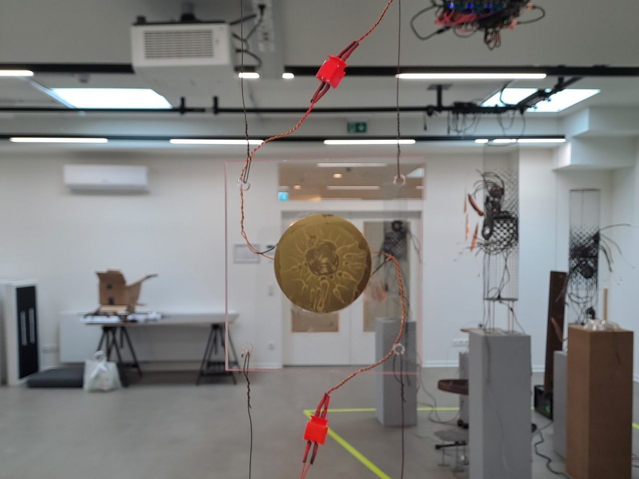 different suspended objects: wooden rings on the left, wooden red square panels in back, glass slides and cables in the front right